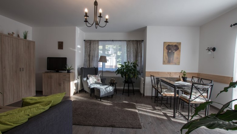 Gem&uuml;tliches Wohnzimmer mit Sofa, Sessel, Esstisch und Pflanzen.