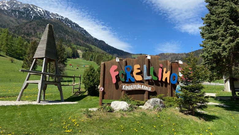 Entrance to the Forellino children's playground with mountain landscape in the background.