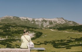 Frau sitzt auf einer Bank und genie&szlig;t den Ausblick auf die Berge beim Damb&ouml;ckhaus am Schneeberg