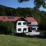 Ein traditionelles Haus mit rotem Dach, umgeben von Wald und Wiese, mit der Aufschrift 'Gschaiderhof'.