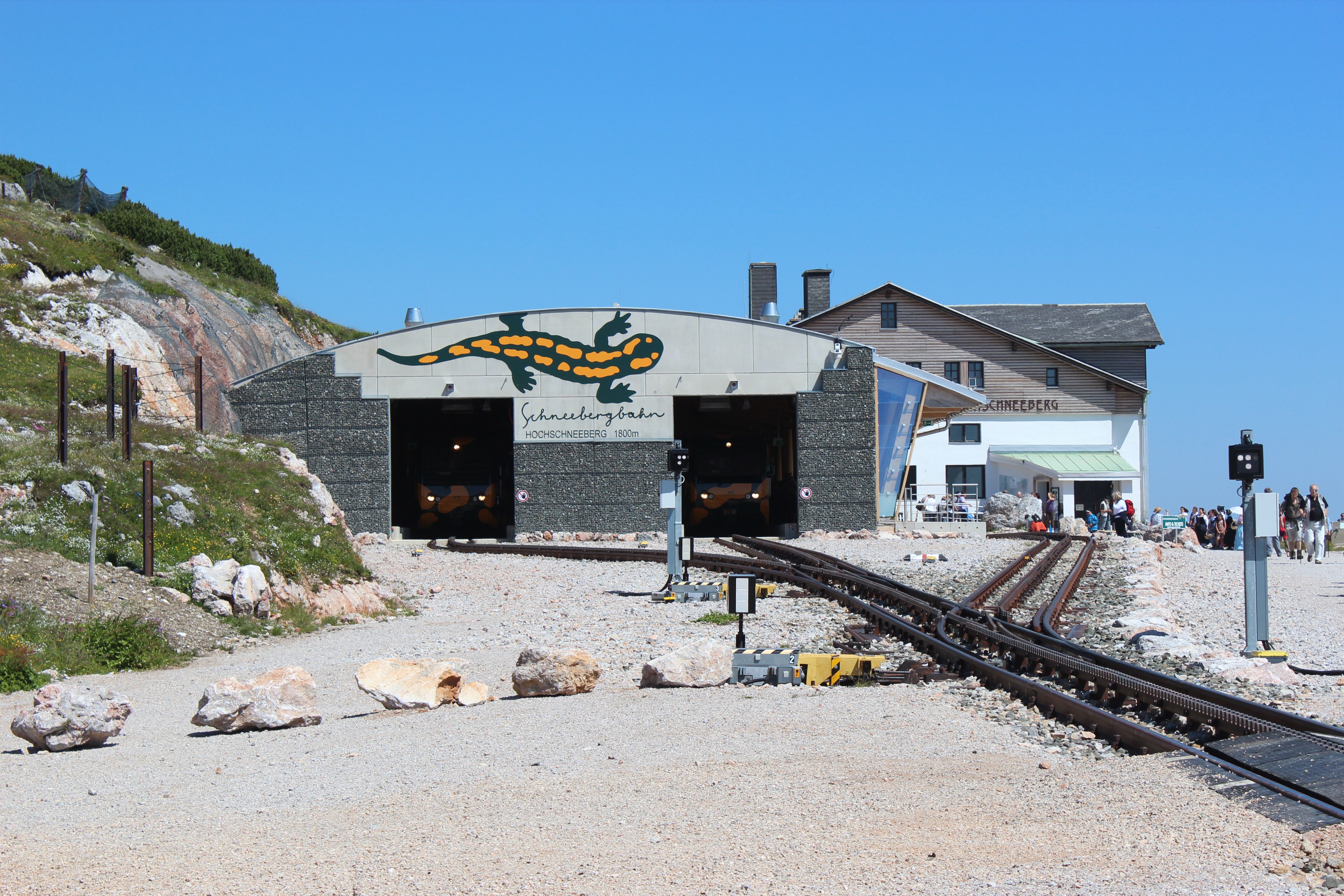 Eingang der Schneebergbahn mit Salamander-Logo und Berghaus im Hintergrund.