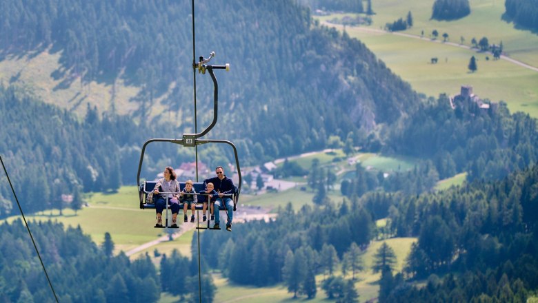 A family rides a chair lift over a green mountain landscape.