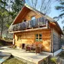 A rustic wooden holiday home with terrace and balcony in a wooded area.