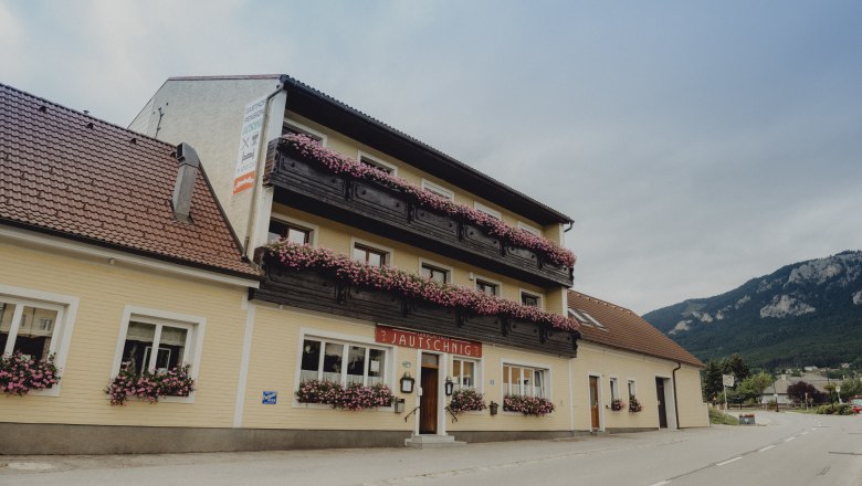 Landgasthof am Fuße der Hohen Wand, © Niederösterreich Werbung/Rita Newman Ein traditioneller Landgasthof mit Blumen geschmückten Balkonen vor einer Bergkulisse.