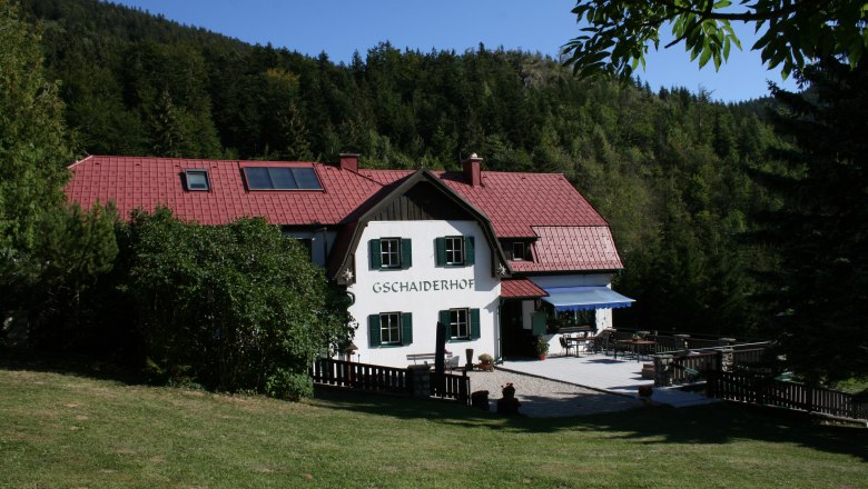 Frühstückspension Gschaiderhof, © Marianne Gschaider Ein traditionelles Haus mit rotem Dach, umgeben von Wald und Wiese, mit der Aufschrift 'Gschaiderhof'.