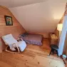 Gem&uuml;tliches Zimmer mit Holzw&auml;nden, einem Bett, einem wei&szlig;en Schaukelstuhl und einem kleinen Tisch.