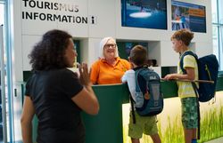 Zwei Jungen mit Rucksäcken im Gespräch mit einer Mitarbeiterin an der Tourismusinformation.