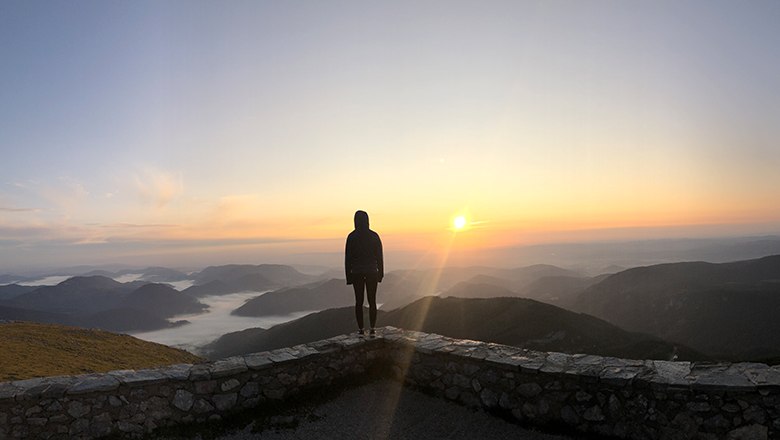 Frau steht auf Mauer und beobachtet den Sonnenaufgang