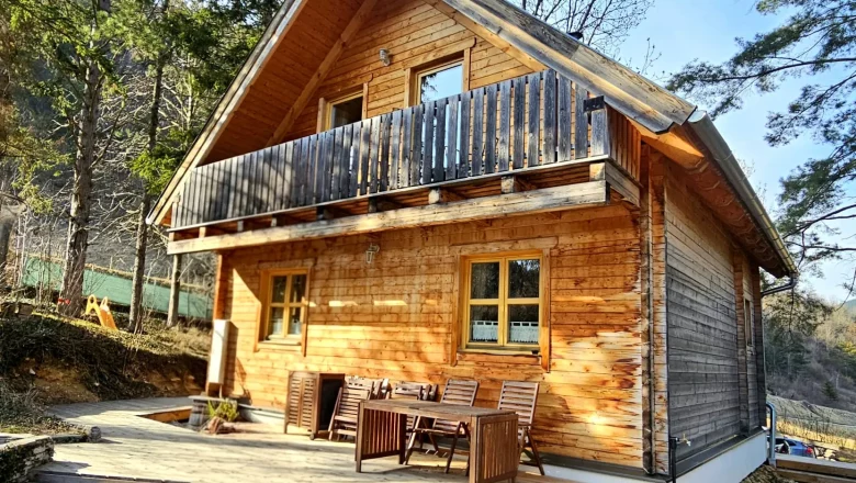A rustic wooden holiday home with terrace and balcony in a wooded area.