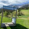 Wooden platform with sign 'Bogenpfad' in front of a mountain landscape.