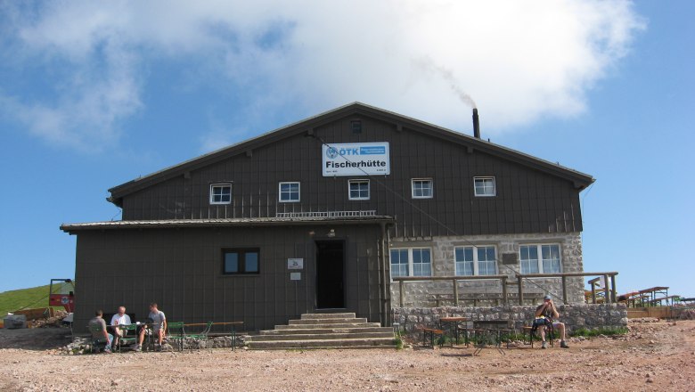 Ein großes Gebäude mit der Aufschrift 'Fischerhütte' vor blauem Himmel.