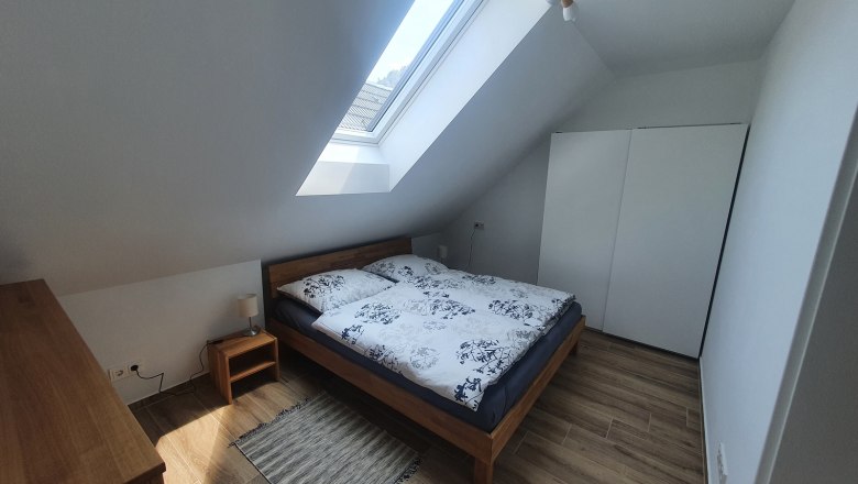 Modern bedroom with skylight, double bed, wooden furniture and white closet.