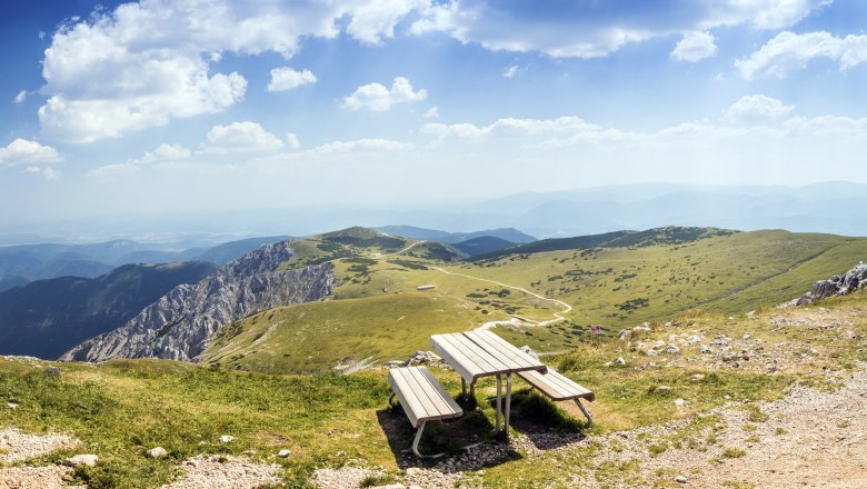 Panoramic view from a mountain with a bench in the foreground and green hills in the background.
