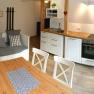 Gem&uuml;tliche K&uuml;che mit Holztisch, wei&szlig;en St&uuml;hlen, Sofa und moderner K&uuml;chenzeile.
