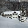 A snow-covered building called Gschaiderhof in front of a forest in winter.