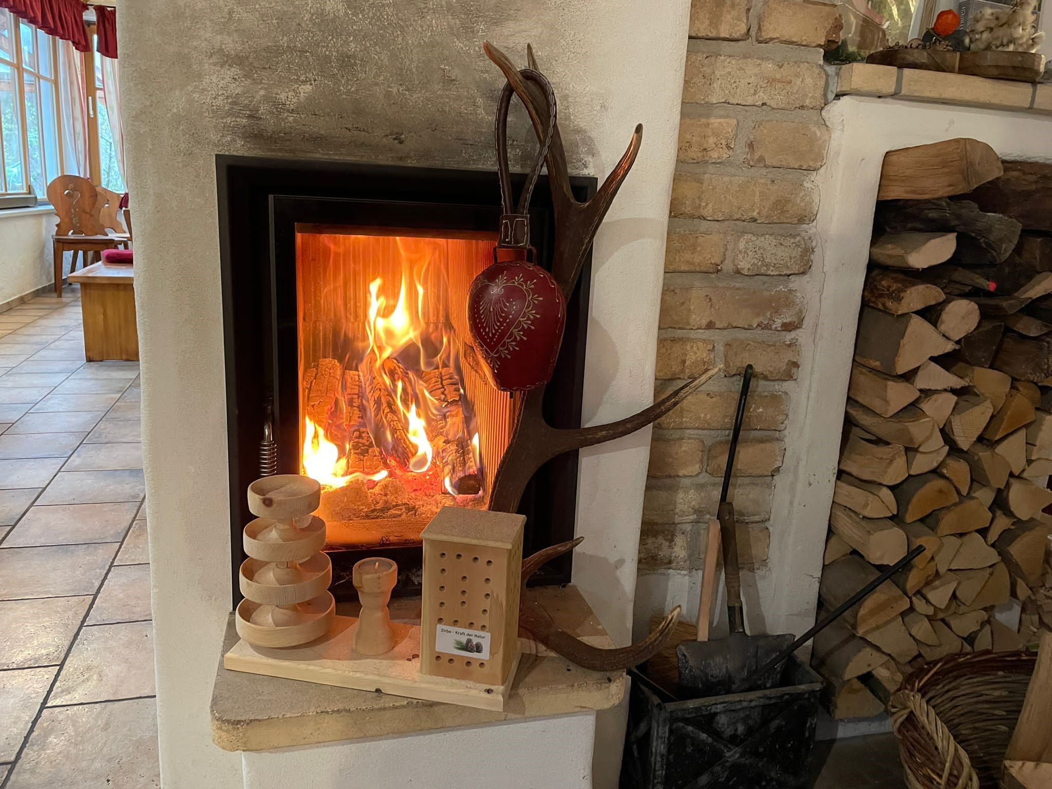 Ein brennender Kamin mit Holzscheiten, Dekorationen und Holzstapel daneben.