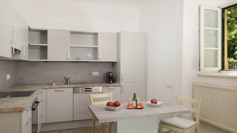 Modern konyha sz&uuml;rke szekr&eacute;nyekkel, asztal alm&aacute;val &eacute;s itallal, nyitott ablak.