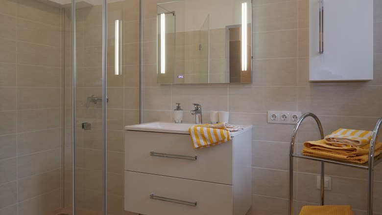 Modern bathroom with shower, washbasin and yellow towels.