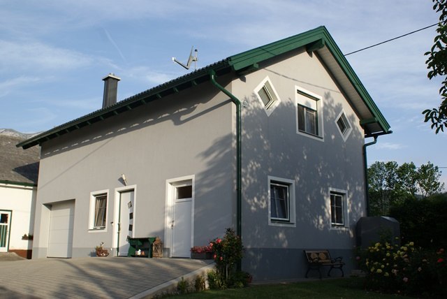 Gray two-story house with green roof and garden bench.