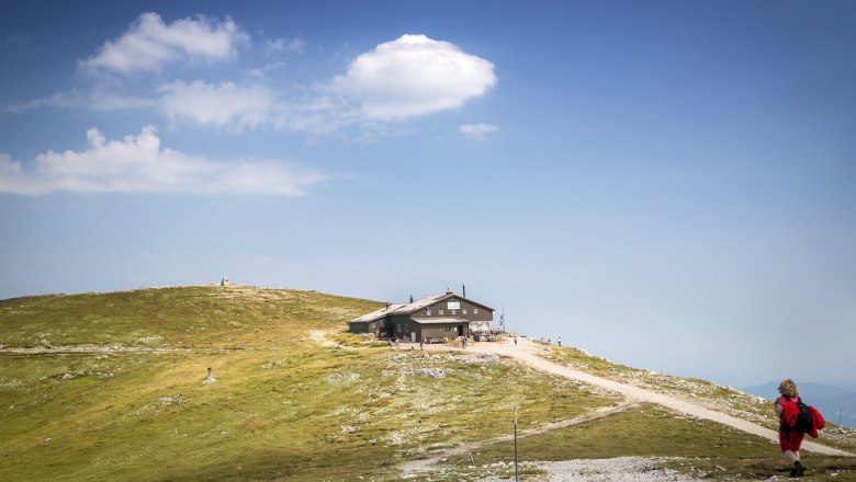 A mountain hut on a hill with a blue sky and clouds in the background.