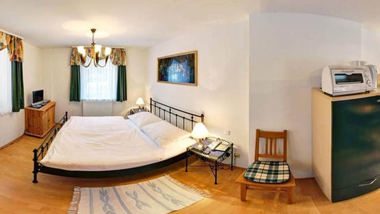 Small bedroom with double bed, bedside tables, TV, microwave and chair.