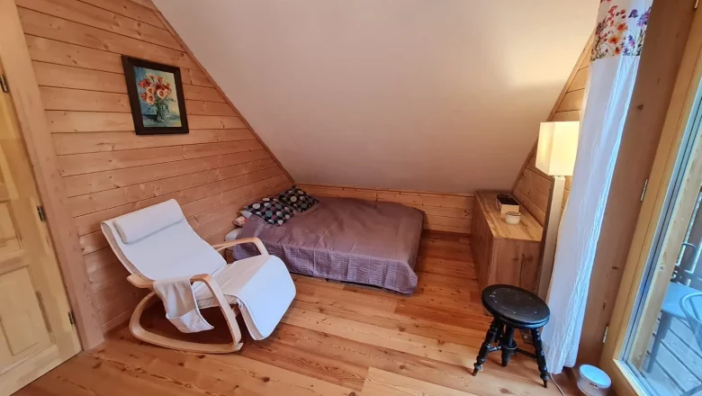 Cozy room with wooden walls, a bed, a white rocking chair and a small table.
