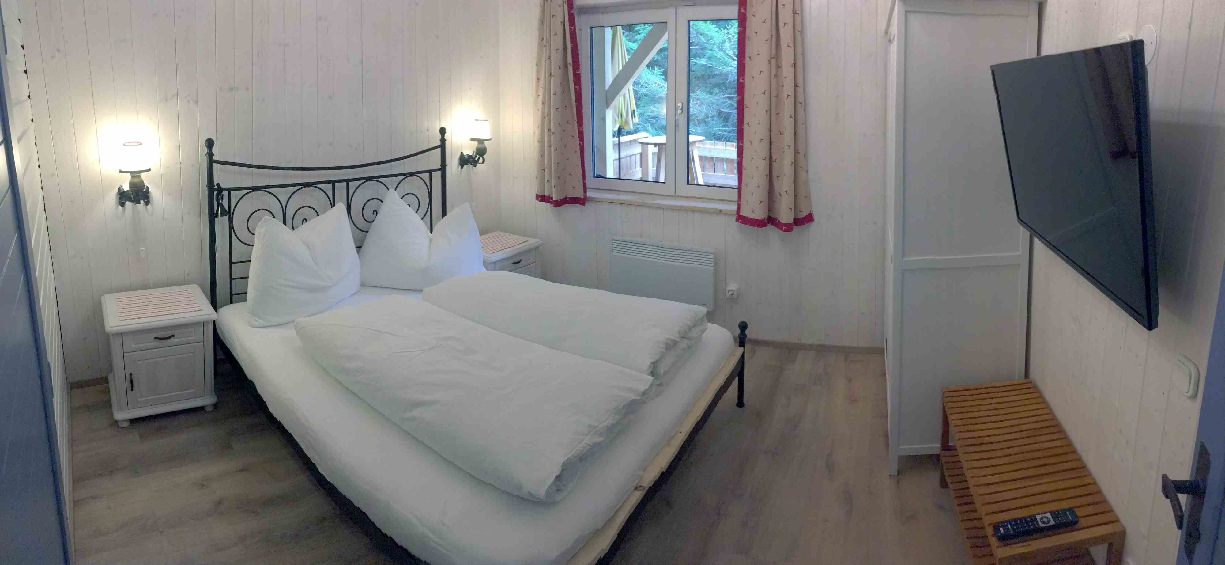 Schlafzimmer in einem Ferienhaus mit Doppelbett, TV und Fenster mit Vorhängen.