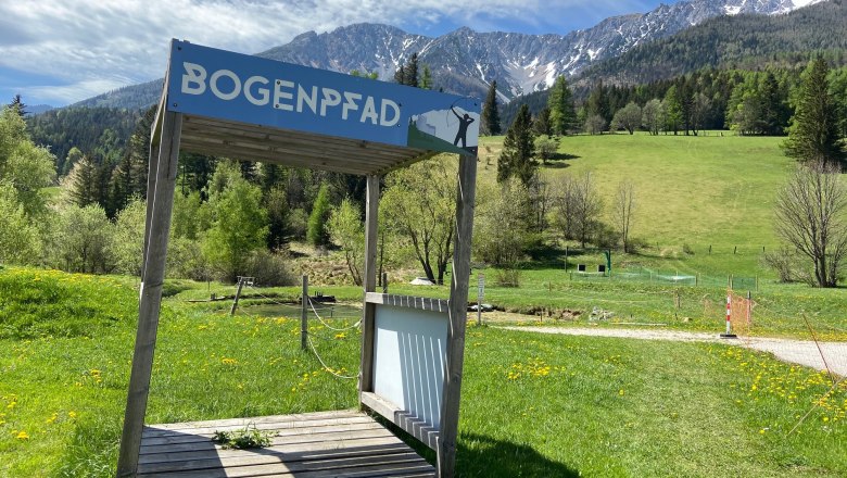 Wooden platform with sign 'Bogenpfad' in front of a mountain landscape.