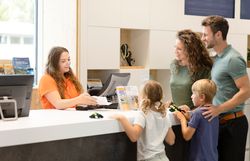 Familie mit zwei Kindern wird an einer Rezeption von einer Mitarbeiterin beraten.