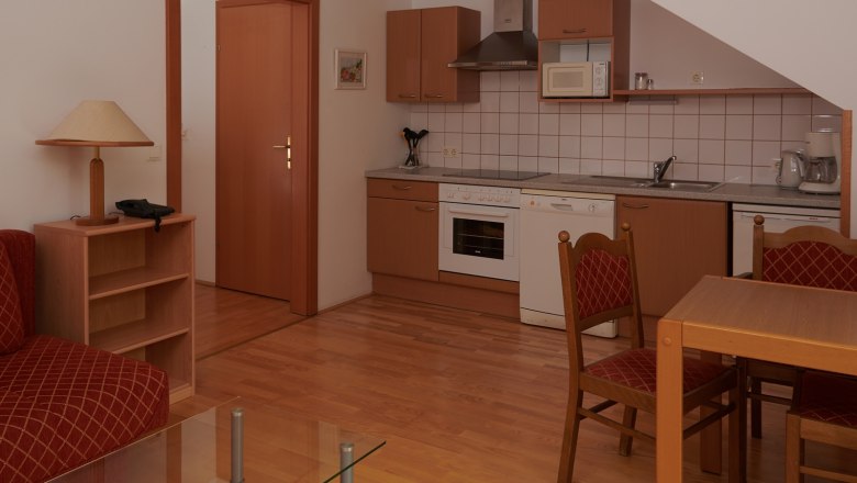 Kompakt konyha fa szekr&eacute;nyekkel, &eacute;tkezőasztallal &eacute;s sz&eacute;kekkel, tűzhely, mosogat&oacute; &eacute;s mikrohull&aacute;m&uacute; s&uuml;tő.