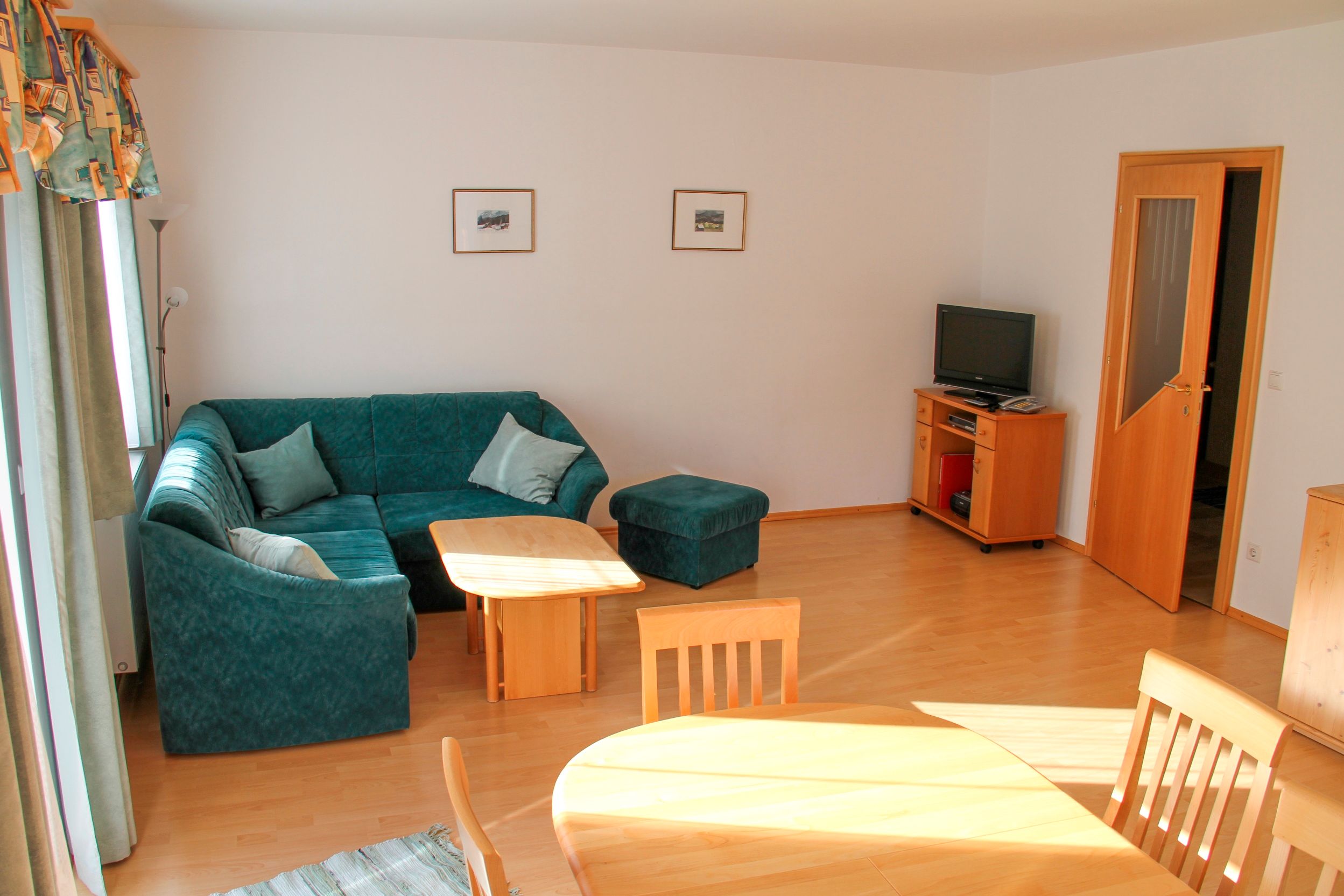 Wohnzimmer mit grüner Eckcouch, Holztisch, Fernseher und Esstisch.