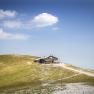 Eine Bergh&uuml;tte auf einem H&uuml;gel mit blauem Himmel und Wolken im Hintergrund.