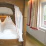 Gem&uuml;tliches Schlafzimmer mit Himmelbett und Balkonblick ins Gr&uuml;ne.