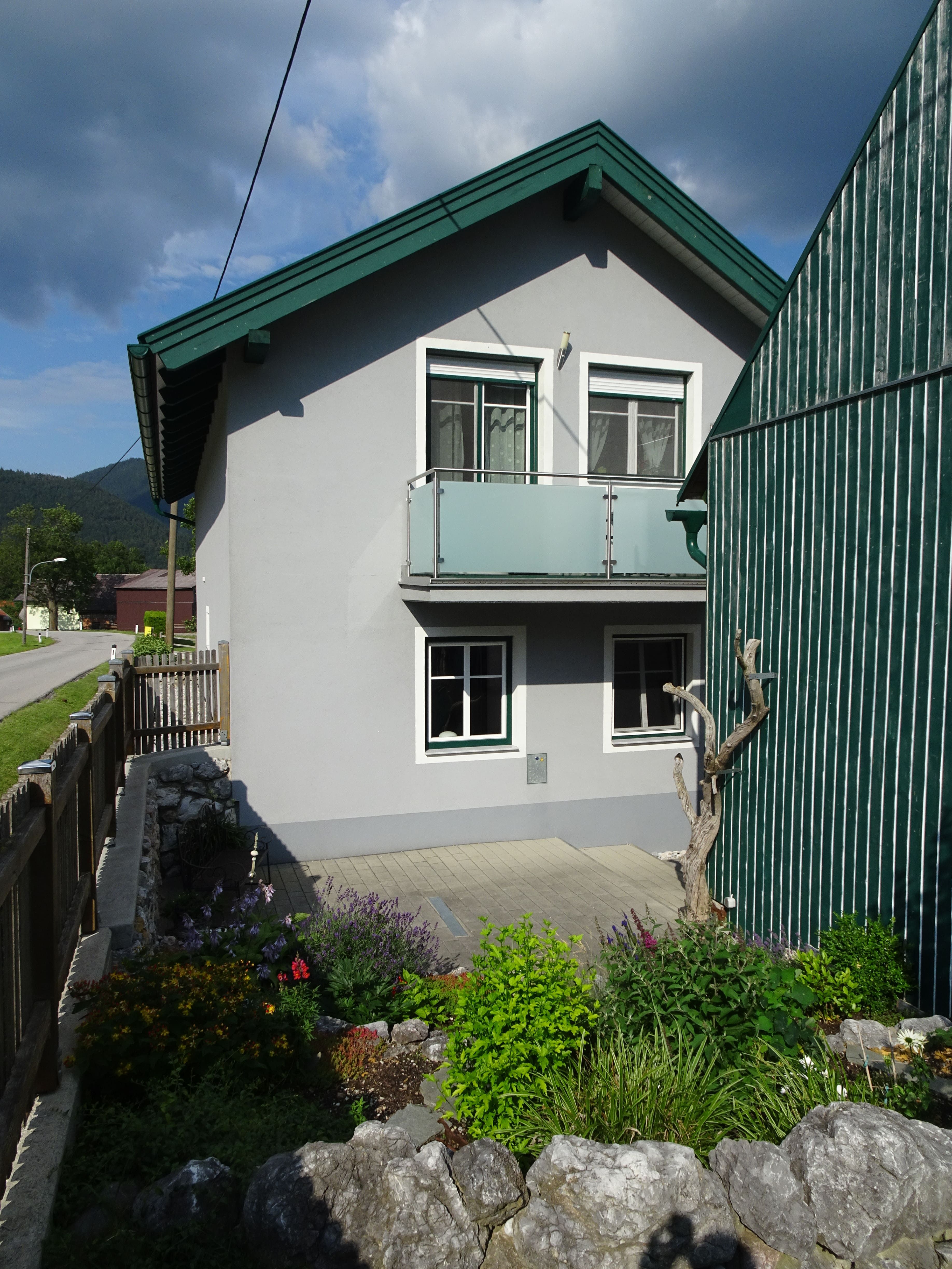 Ein graues Haus mit grünem Dach und kleinem Garten im Vordergrund.