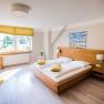 Helles Doppelzimmer mit Holzbett, gelben Kissen und gro&szlig;em Fenster.