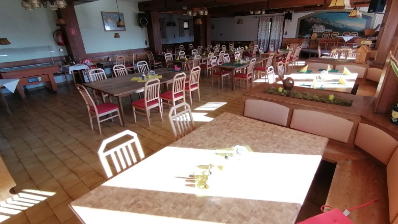 Egy &uuml;res &eacute;tkezőterem, faasztalokkal &eacute;s piros sz&eacute;kekkel a Gasthof Mohrban.