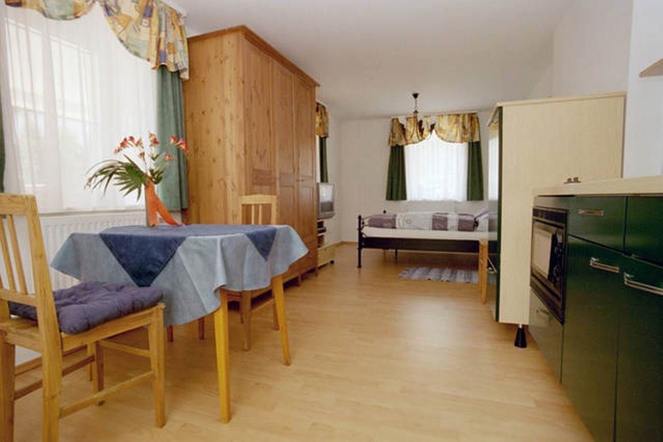 Kleine Wohnung mit Holzmöbeln, Esstisch, Stühlen, Bett und Küchenzeile.