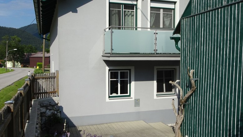 A gray house with a green roof and a small garden in the foreground.