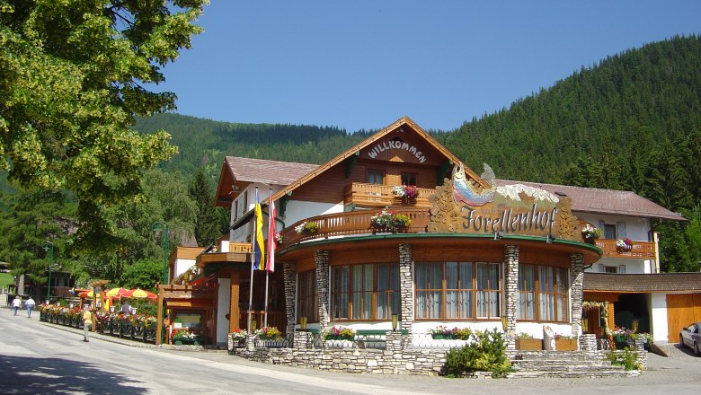 Ein traditionelles Hotel mit Holzfassade und Blumen, umgeben von Bergen und Bäumen.
