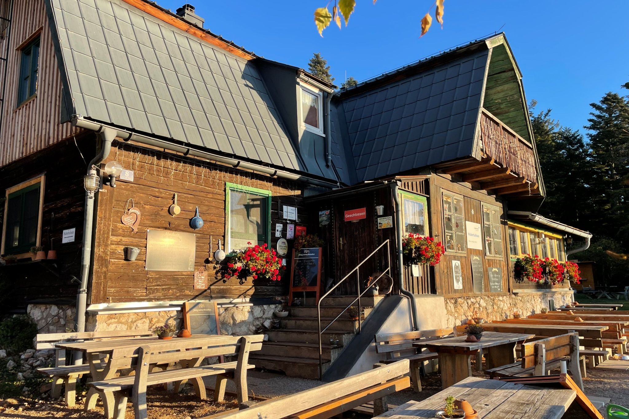 Ein rustikales Holzhaus mit Blumen und Sitzbänken im Freien bei Sonnenschein.