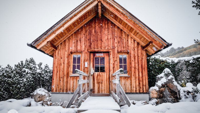 Eine kleine Holzh&uuml;tte im Schnee mit einem steilen Dach und zwei Fenstern.