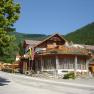 A traditional hotel with a wooden façade and flowers, surrounded by mountains and trees.