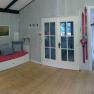 Innenansicht eines gem&uuml;tlichen Ferienhauses mit Holzboden, rotem Sofa, Skiern an der Wand und Glast&uuml;ren.